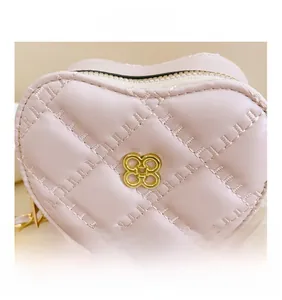 Detailed close-up of pink quilted heart bag with golden petal logo and chain strap