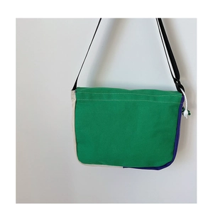 Détail du sac messager en toile verte avec sangle réglable et coutures colorées
