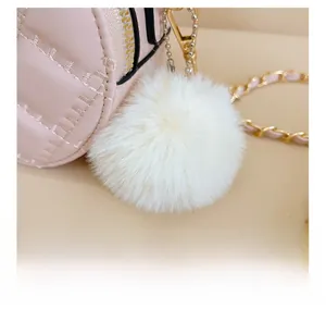 Macro shot of pink quilted leather bag with fluffy white pompom charm and gold chain strap