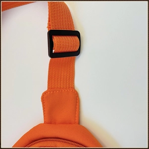 Détail de la boucle réglable en plastique noir et de la sangle en toile orange pour enfant