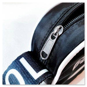 Macro shot of durable black nylon crossbody bag with white piping and metallic zipper