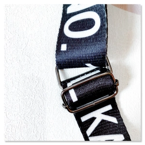 Detail of adjustable metal buckle on black crossbody strap with white letters