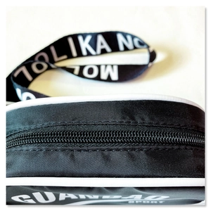 Detailed macro view of black sport crossbody bag with resin zipper and branded webbing strap