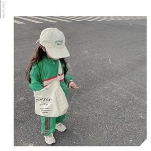 Detail of a large beige canvas crossbody bag styled with a green kids' tracksuit