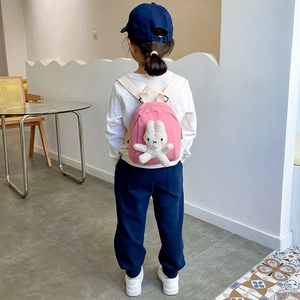 Pink canvas toddler backpack with a white plush bunny doll, shown from a rear model view