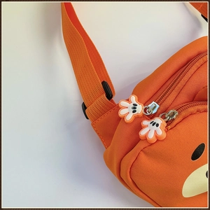 Détail du sac de poitrine ours orange avec fermeture gant blanc et texture en toile