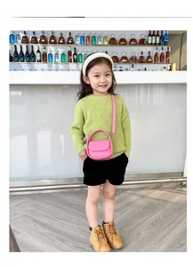 Girl's mini pink saddle bag with top handle and strap shown on model in a cozy indoor setting