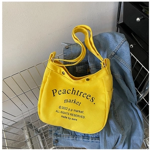 Detail of yellow canvas crossbody bag with black vintage letters on a blue denim background