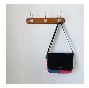 Détail d'un sac messager en toile contrastée suspendu sur un mur blanc minimaliste