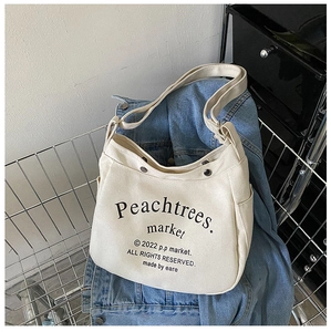 Detail of canvas shoulder bag with metal snap button and lettering in a shopping basket