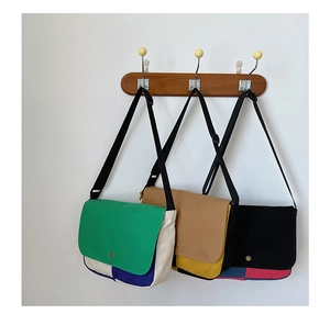 Détail de sacs bandoulière en toile colorée suspendus à des crochets en bois sur mur blanc