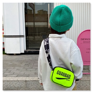 Detailed street style view of fluorescent green kids crossbody bag with black letter strap