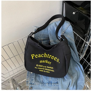 Detail of black canvas shoulder bag with yellow text inside a metal shopping cart