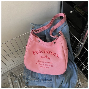Detail of pink canvas crossbody bag with red typography in a lifestyle shopping scene