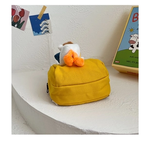 Detail of yellow canvas backpack featuring a cartoon duck plush pendant and black zipper