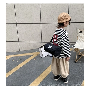 Detail of a black quilted cylindrical bucket bag with a minimalist white side label