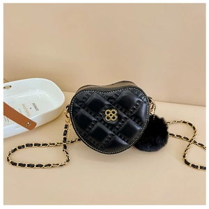 Detail of black heart-shaped quilted bag featuring golden floral clasp and pom-pom charm