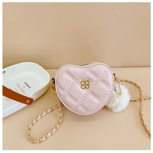 Detail of pink heart-shaped quilted crossbody bag with gold chain and plush ball charm