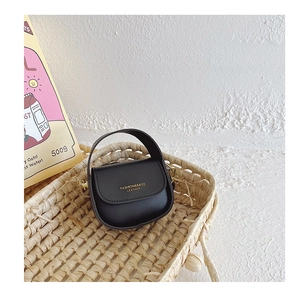 Close-up of black mini PU leather girl's handbag with gold lettering on a woven tray