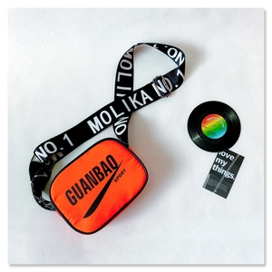 Flat lay of bright orange crossbody bag with black graphics and lettered strap details