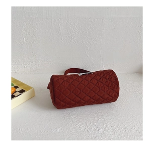 Detail view of brick red quilted bucket bag featuring diamond stitching and white woven label