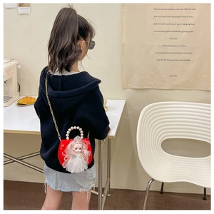 Detail showing red girl's mini bag with doll decor, pearl handle and gold chain strap
