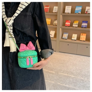 Detail of mint green quilted crossbody bag with large pink bow and metal chain strap