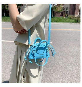Close-up of bright blue mini shell bag with leather texture and drawstring inner pouch