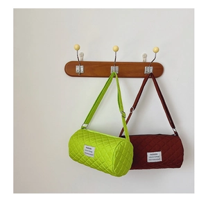 Close-up of quilted cylinder bucket bags in neon green and burgundy on wooden wall hooks