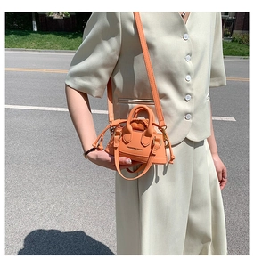 Detail view of an orange mini crossbody bag with drawstring sides and dual top handles