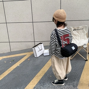 Kids black quilted cylinder crossbody bag shown on a model in an outdoor fashion setting