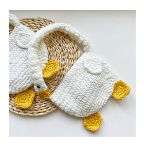 Detailed view of handmade crochet white goose earmuffs on a woven mat background