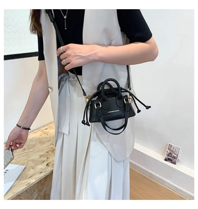 Detail of a mini black faux leather shell bag with gold branding and drawstring closure