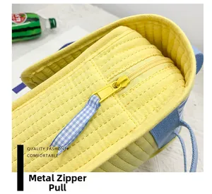 Close-up of metal zipper puller on yellow quilted fabric bag with blue checkered ribbon
