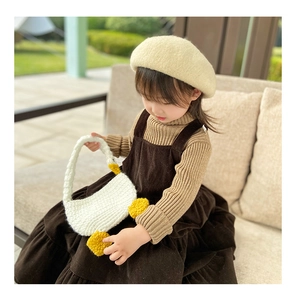 Detail of hand-knitted white goose bag paired with brown corduroy dress and knit hat