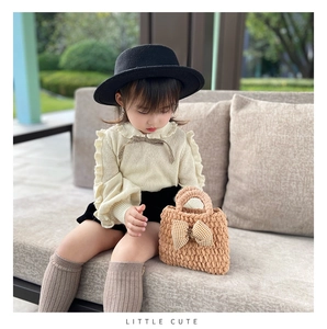 Detail of a khaki knitted toddler tote bag with a yellow checkered bow on a plush texture