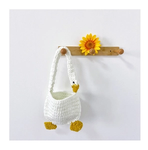 Detail of handcrafted crochet white goose bag hanging on a wooden hook with a sunflower