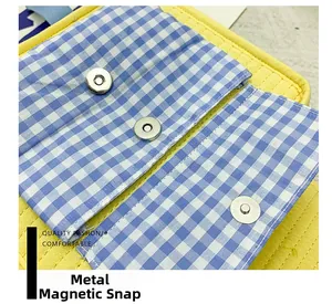 Close-up of magnetic snap closures on yellow canvas backpack with blue gingham lining
