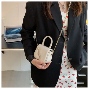 Mini cream crossbody bag with wavy flap design shown on model with gold chain strap