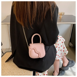 Pink mini crossbody bag with wave design and gold chain worn with black blazer