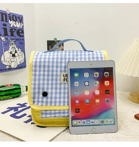 Blue and white checkered kids bag with yellow trim and button closure next to a tablet