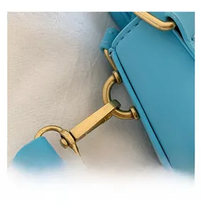 Detail of the golden hardware hook and blue leather stitching on the shell crossbody bag
