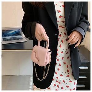 Pink mini crossbody bag with wavy flap and gold chain strap held by a stylish model