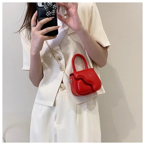 Close-up of a glossy red mini handbag with gold chain strap worn with a cream suit
