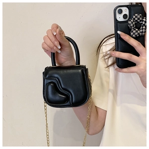 Detail of mini black crossbody bag with heart relief and elegant gold chain strap