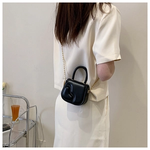 Close-up of black mini bag with wavy texture and golden chain strap in a casual setting