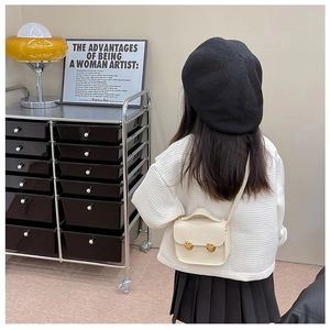 Vue de dos d'un enfant portant un mini sac bandoulière crème avec un haut en maille gaufrée