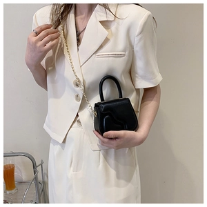 Mini black handbag with wavy flap and gold chain strap worn with cream suit