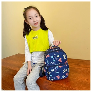 Detail view of child wearing a navy blue canvas backpack with cute cartoon dinosaur prints