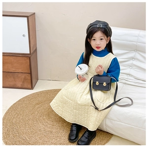 Fille en robe matelassée jaune et pull bleu avec un mini sac carré noir à la main